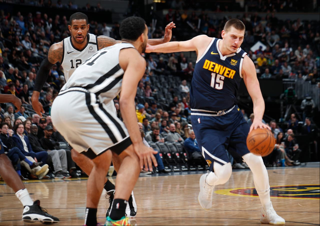 El centro de los Denver Nuggets Nikola Jokic conduce el balón hasta la canasta pese a la marca de Trey Lyles y LaMarcus Aldridge de los San Antonio Spurs.